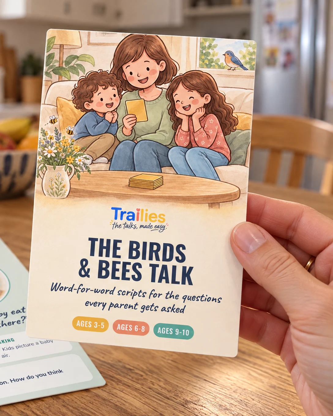 A parent holding up The Birds & Bees Talk cover card in a kitchen