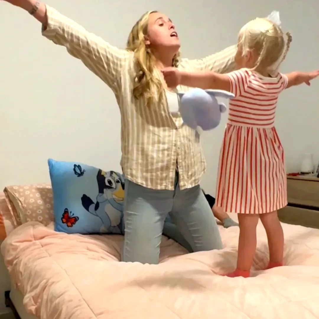 A mom and her daughter playing with arms outstretched on the bed